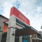 The Market at Waterside brick facade with a red sign reading "MARKET" under a cloudy sky, with a street lamp beside it.