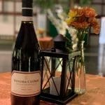 A bottle of Sonoma-Cutrer Russian River Valley Pinot Noir beside a black lantern and a vase of orange flowers.