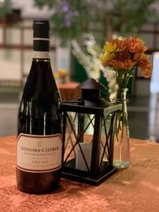 A bottle of Sonoma-Cutrer Russian River Valley Pinot Noir beside a black lantern and a vase of orange flowers.