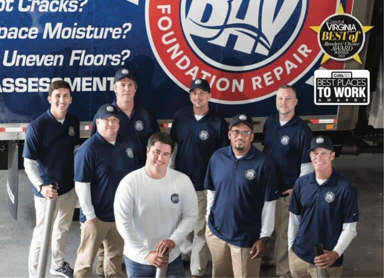 Seven men in navy polo shirts and white long-sleeve shirts pose before a truck reading "Bay Foundation Repair.