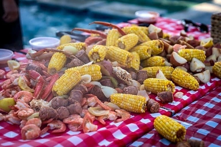 A spread of seafood boil on a red-and-white checkered tablecloth with shrimp, corn on the cob, sausage, potatoes and crab legs.