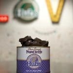 A 16-ounce tin of Hubs Choco Covered Peanut Brittle from Hubbard Peanut Company, with chocolate pieces spilling over the top.