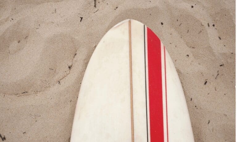 A white surfboard with red and thin pinstripes lies nose-first in the sand.