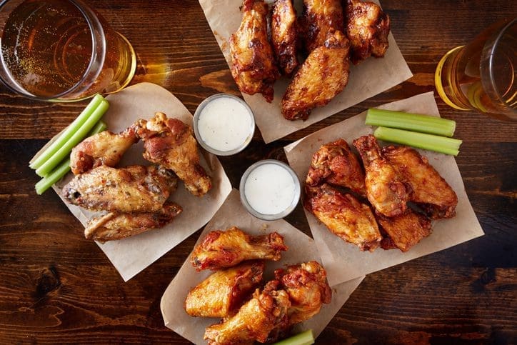 overhead view of four different flavored chicken wings with ranch dressing, beer, and celery sticks