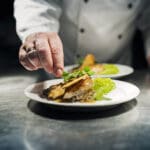 Professional chef putting the final flourish to the dish by adding a sprig of watercress to the dish of slow cooked chicken b