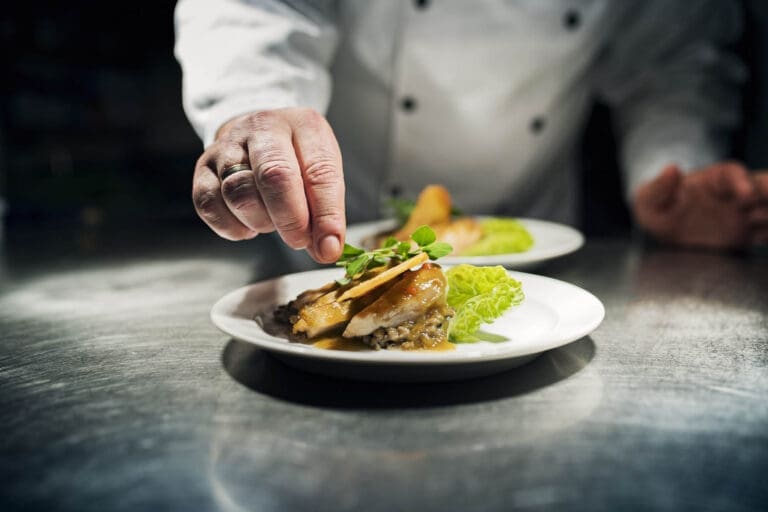 Professional chef putting the final flourish to the dish by adding a sprig of watercress to the dish of slow cooked chicken b