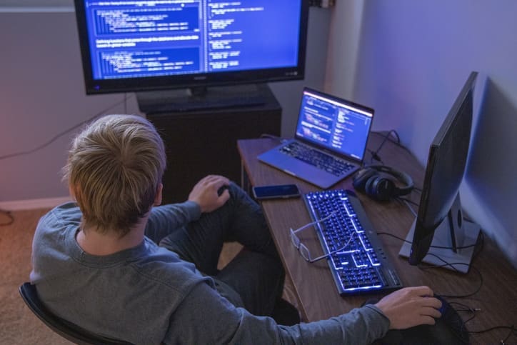 He works in a home office and is illuminated by the computer screens