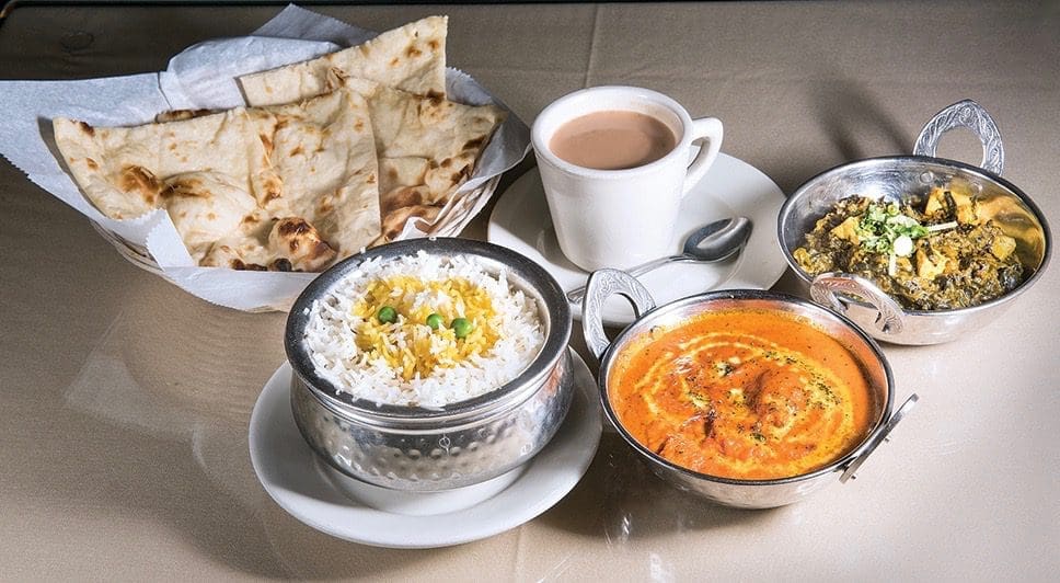 Basket of naan, a cup of chai, and steel bowls of rice, orange tikka masala, and creamed spinach.