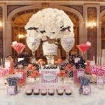 A candy buffet with white roses, pink and navy striped sweets, macarons, cupcakes, and lollipops on a white table.