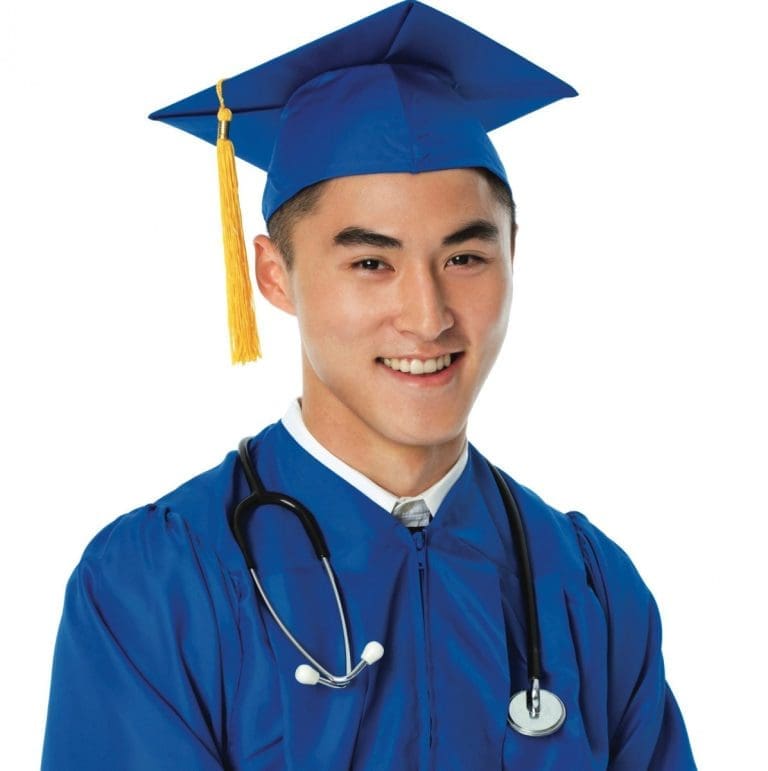 A smiling young man in a royal blue graduation cap and gown with a gold tassel and a stethoscope around his neck.