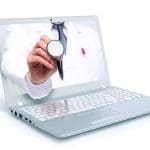 A silver laptop screen shows a doctor in a white coat holding a stethoscope toward the viewer.