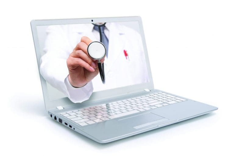 A silver laptop screen shows a doctor in a white coat holding a stethoscope toward the viewer.