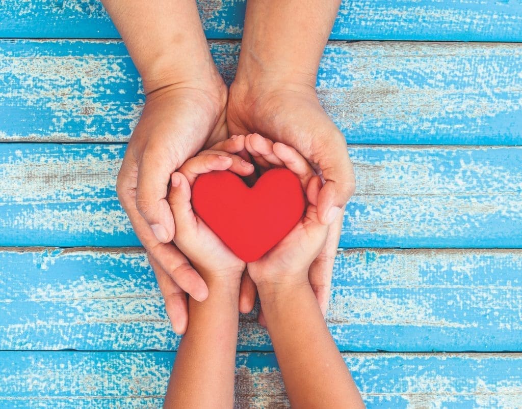 Red heart in child kid and mother hands on old blue wooden table in vintage retro style