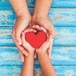 Red heart in child kid and mother hands on old blue wooden table in vintage retro style