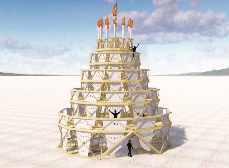 A tiered, multi-level sculpture of gold lattice and white panels topped with flaming torches, with silhouetted figures on a white desert playa.