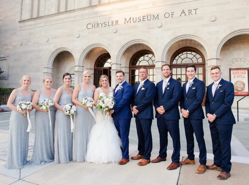 A bride and groom posing with bridesmaids in gray gowns and groomsmen in navy suits before the Chrysler Museum of Art.