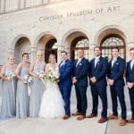 A bride and groom posing with bridesmaids in gray gowns and groomsmen in navy suits before the Chrysler Museum of Art.