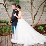 A bride in a strapless tulle gown leans against a groom in a dark military dress uniform, standing back to back.