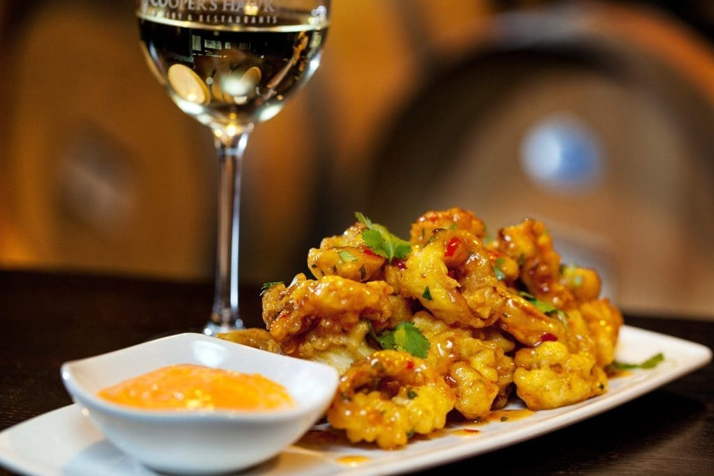 Crispy glazed bites garnished with cilantro, served with orange dipping sauce beside a glass of white wine.