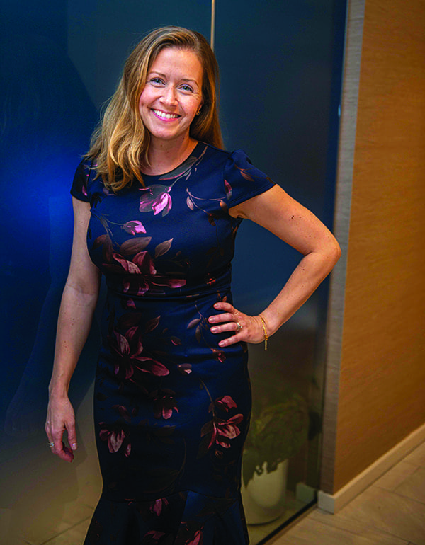 Allyson McNaughton smiles with one hand on her hip, wearing a navy dress with pink floral print.