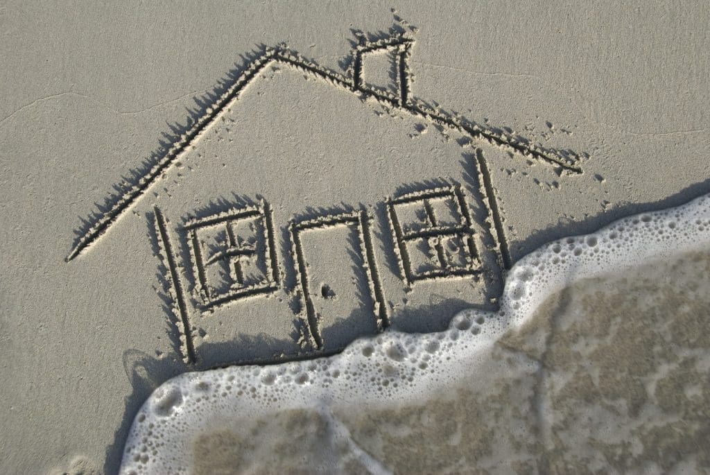 House in the sand is overtaken by a foamy wave; focus on sand and motion blur on the wave