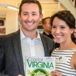 Two smiling people stand indoors holding a Coastal Virginia Magazine issue with the headline "Boosting Brain Health.