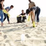 Group Of Volunteers Tidying Up Rubbish On Beach Holding Plastic Bags.