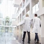 Rear View Of Doctors Talking As They Walk Through Hospital