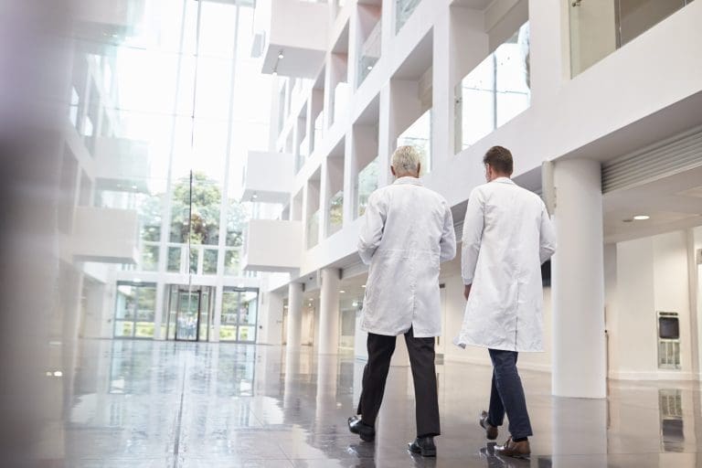 Rear View Of Doctors Talking As They Walk Through Hospital