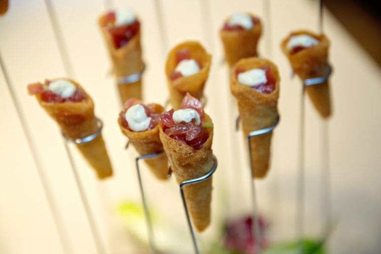 Crispy cone-shaped wafers holding diced red tuna and a dollop of cream, displayed on thin metal wire stands.