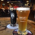Two pint glasses of beer on a wooden barrel table, one dark stout and one golden ale, branded Isley Brewing Company, Richmond, VA.