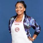 Smiling woman with long braids in a galaxy-print bomber jacket and white MasterChef apron reading EBONI, hand on hip.