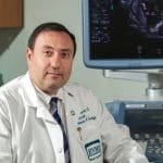 Dr. Alfred Abuhamad in a white coat beside an ultrasound machine, with an EVMS logo on his coat.