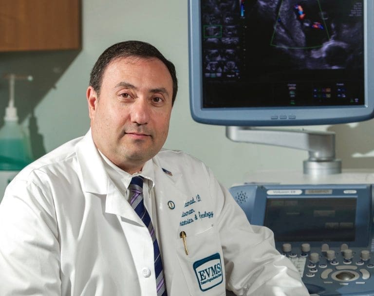 Dr. Alfred Abuhamad in a white coat beside an ultrasound machine, with an EVMS logo on his coat.