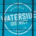 Teal window panes display a white circular logo reading "Norfolk Virginia" around "Waterside District" in distressed lettering.