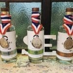 Three small-batch spirit bottles labeled Vodka, Gin and Single Malt, each with a medal on a red, white and blue ribbon.