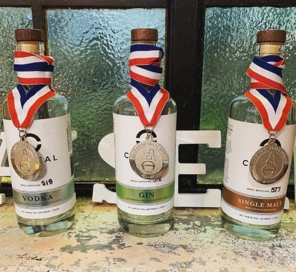 Three small-batch spirit bottles labeled Vodka, Gin and Single Malt, each with a medal on a red, white and blue ribbon.