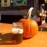 A mason jar of Back Bay Brewing beer beside a pumpkin, with Steel Pier and Atlantic Ale signs behind.