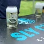A frothy beer glass branded "CoVa Battle of the Burgers" sits on a black table with blue "SLY CLYDE" lettering.