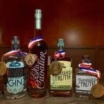 Four craft spirit bottles with gold medals and red, white, and blue ribbons: Fourth Handle gin, Chevalier bourbon, Tarnished Truth rye and mash.