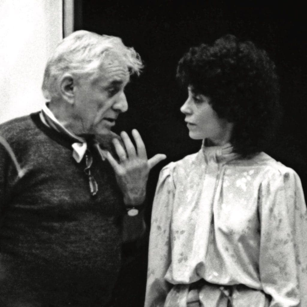 Black-and-white photo of an older man with white hair gesturing as he speaks to a woman with dark curly hair in a blouse.