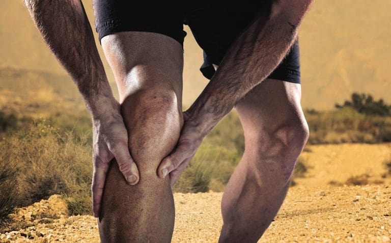 young sport man with strong athletic legs holding knee with his hands in pain after suffering muscle injury during a running