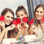 Picture presenting three girlfriends holding hearts in cafe