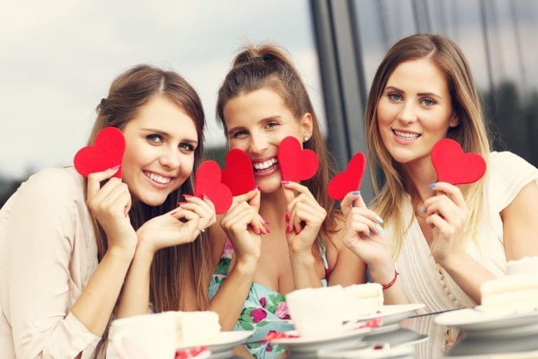 Picture presenting three girlfriends holding hearts in cafe