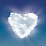 A white, fluffy cloud shaped like a heart against a blue sky with sunburst rays.