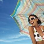 Young woman holding beach umbrella, smiling, close-up