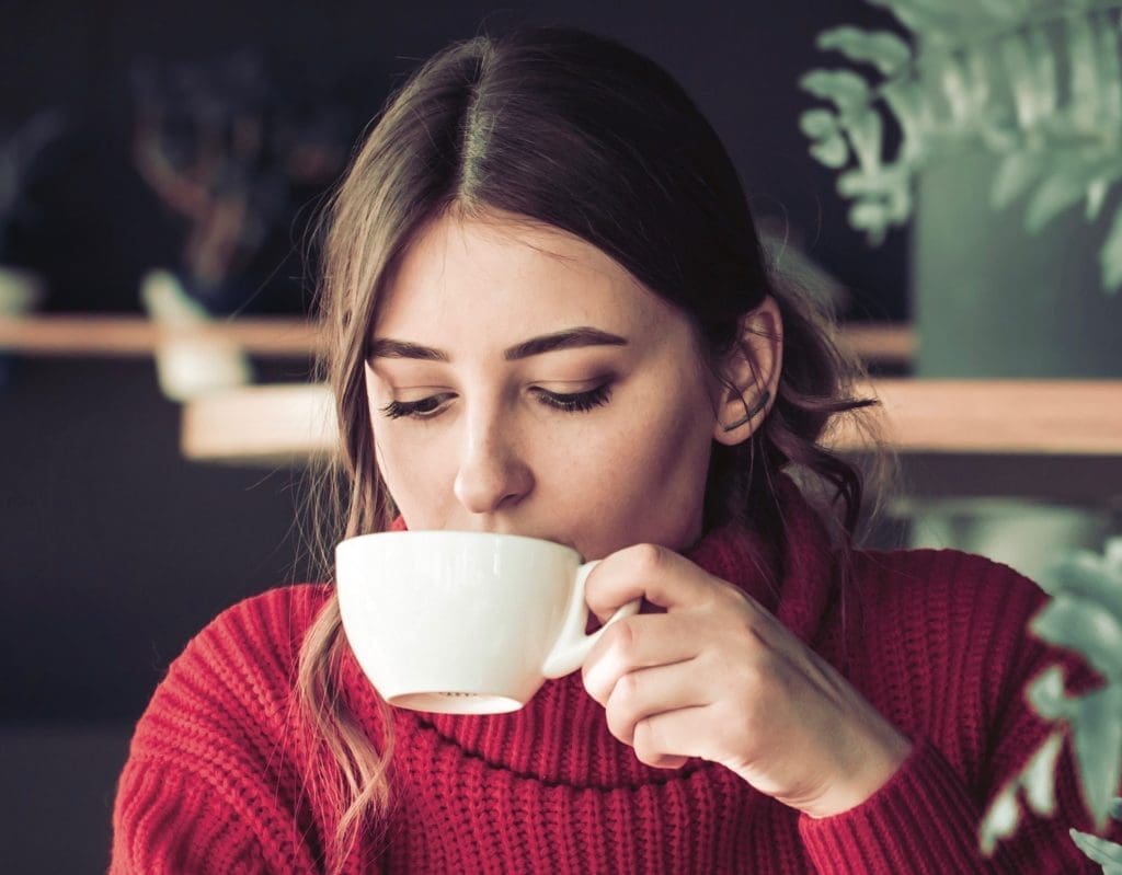 A beautiful girl in a red knitted sweater drinks tea and reads a book in a cozy cafe, the concept of pleasant leisure and com