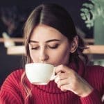 A beautiful girl in a red knitted sweater drinks tea and reads a book in a cozy cafe, the concept of pleasant leisure and com