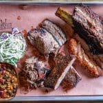 A barbecue platter on butcher paper with brisket, pulled pork, ribs, sausage, coleslaw, and baked beans, with a Redwood Smoke Shack logo.