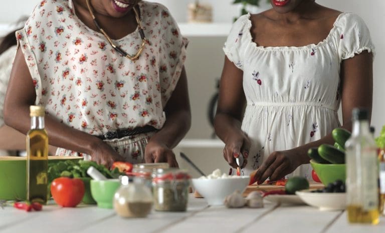 Two unrecognizable african women cooking in kitchen making healthy food salad with vegetables